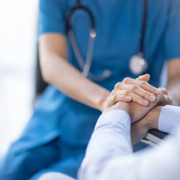 Nahaufnahme einer Ärztin in blauer Uniform mit Stethoskop, die die Hand eines Patienten hält. Nahaufnahme einer Ärztin in blauer Uniform mit Stethoskop, die die Hand eines Patienten hält.
